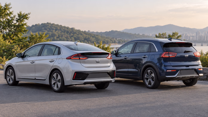 Серебристый Hyundai Ioniq Hybrid и синий Kia Niro DE у озера — синтетическая редакционная иллюстрация