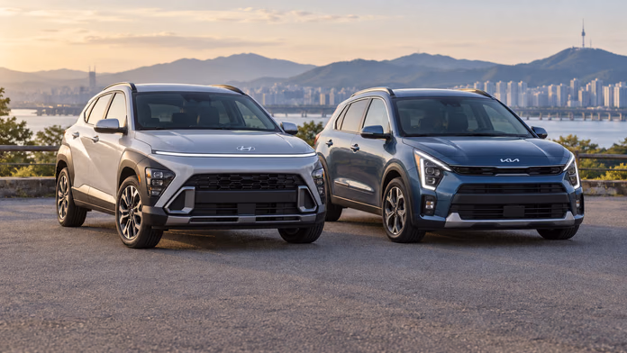 Hyundai Kona и Kia Niro на площадке у реки и городских холмов; синтетическая редакционная иллюстрация