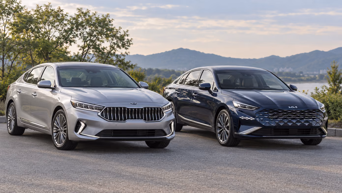 Серебристый Kia K7 Premier и синий Kia K8 у озера — синтетическая редакционная иллюстрация