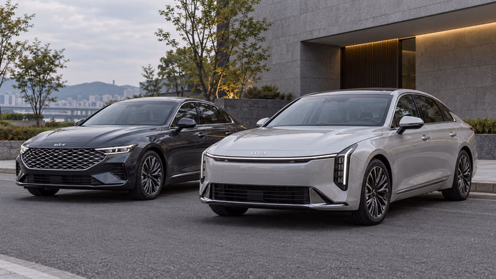 Дорестайлинговый серый Kia K8 и серебристый обновлённый K8 у здания — синтетическая редакционная иллюстрация