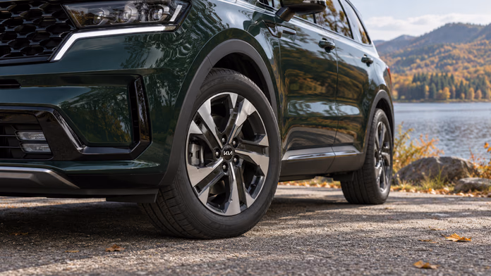 Переднее колесо и боковина шины тёмно-зелёного Kia Sorento MQ4 у озера — синтетическая редакционная иллюстрация