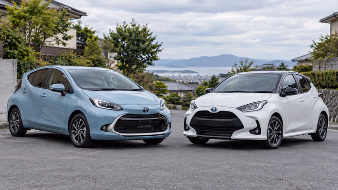 Голубая Toyota Aqua и белый Yaris на тихой улице; синтетическая редакционная иллюстрация.